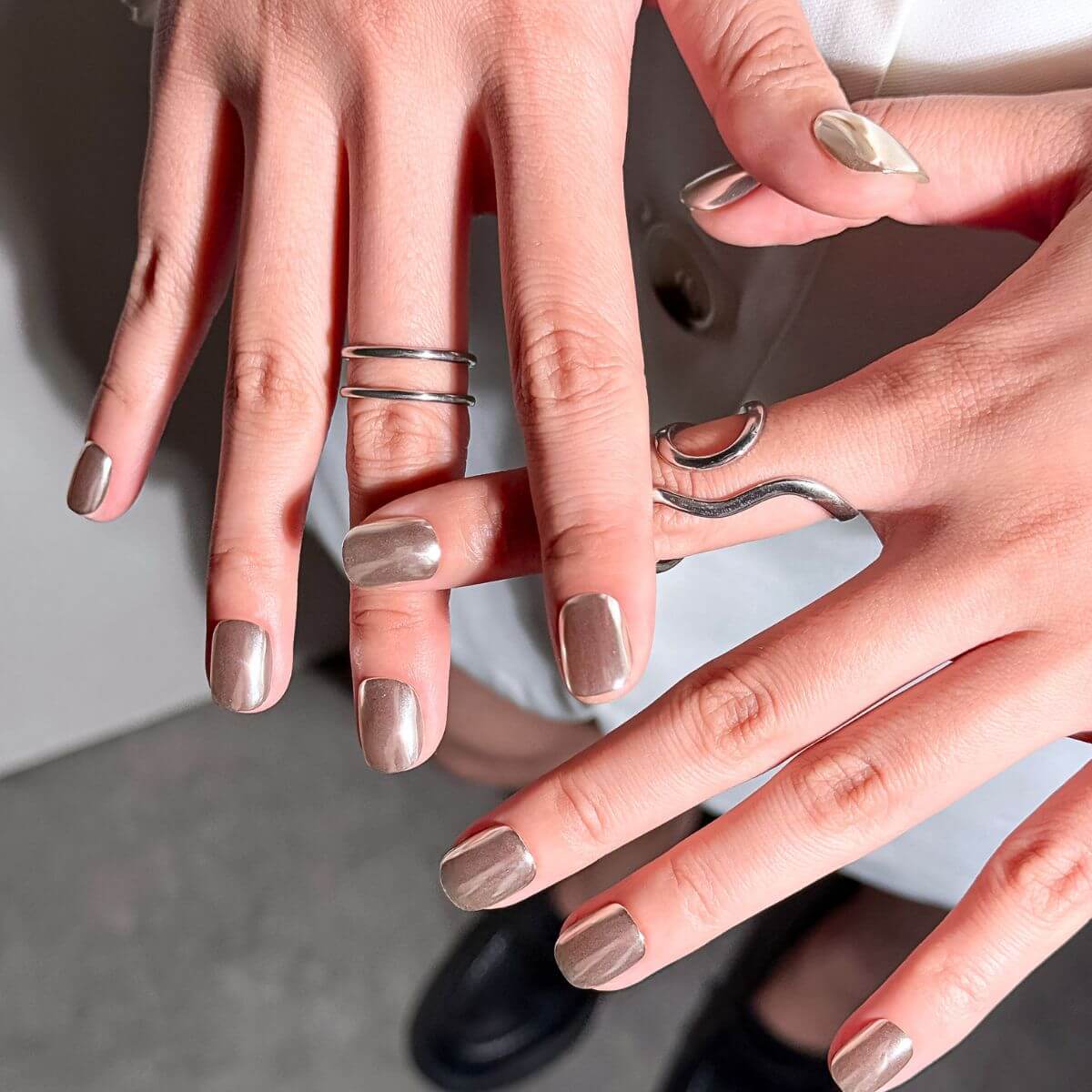 Lifestyle shot of a hand wearing justmee Modern Minimalist silver chrome nails. Highlights the reflective metallic finish and minimalist gel nail aesthetic.