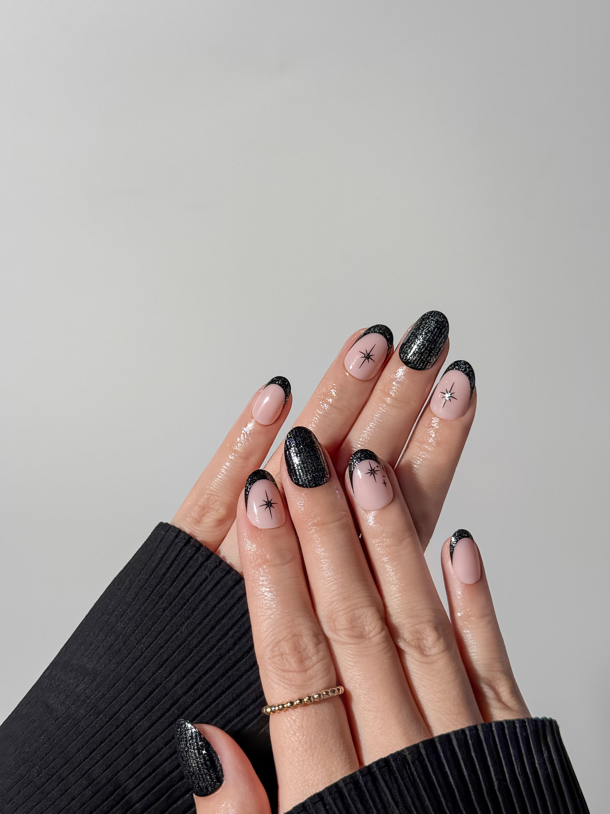 Hand wearing short round black glitter French tip nails with hand-painted starburst motifs