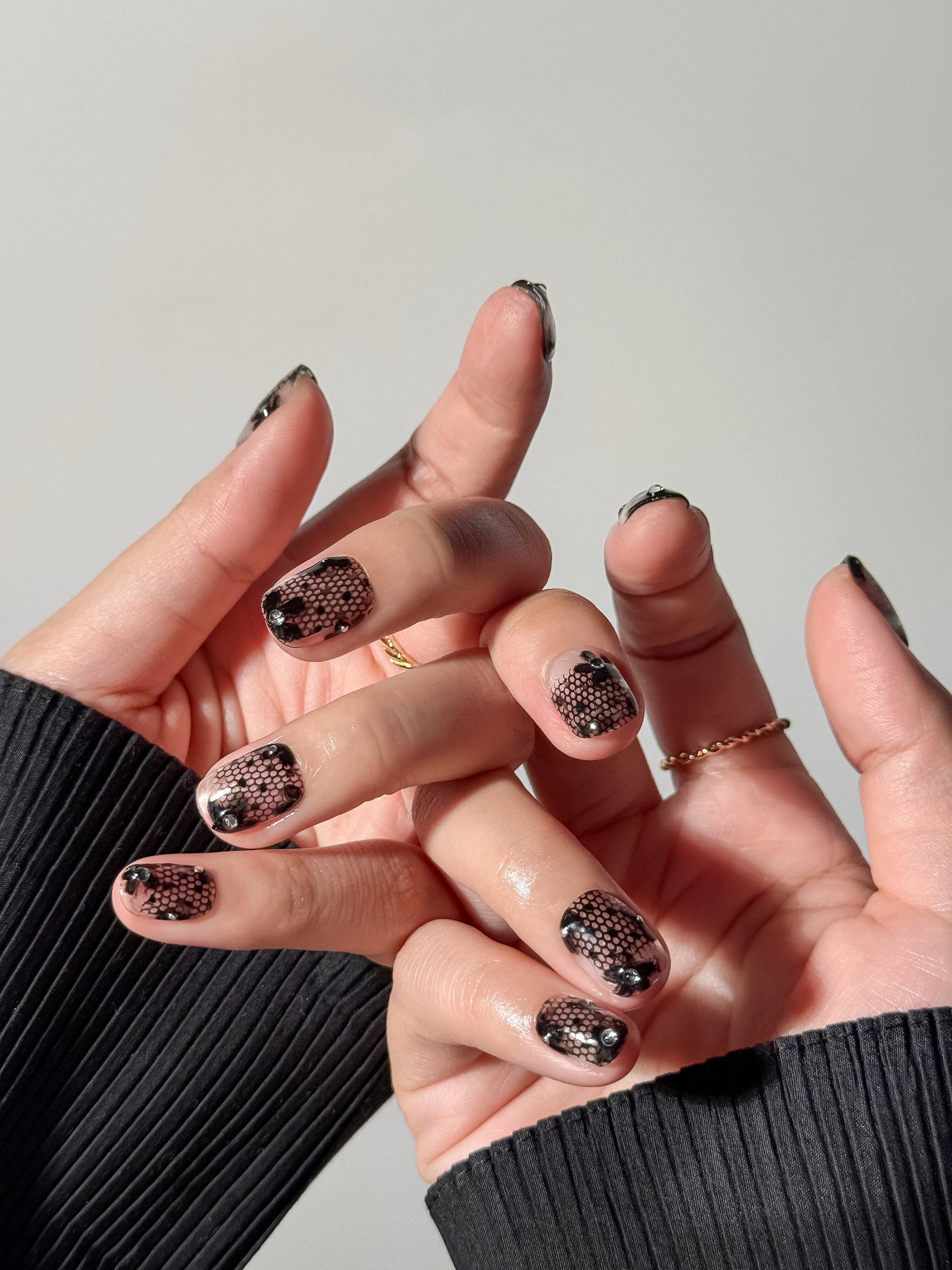 Hand model wearing short square transparent nails featuring intricate black lace designs, perfect for date or special occasions like valentine's day