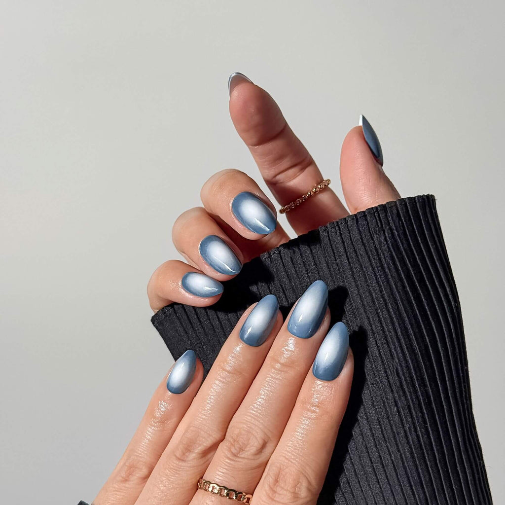 Detailansicht einer Hand mit mittellangen mandelförmigen Nägeln, die einen blauen magnetischen Samtschimmer-Effekt und ein leuchtendes Aura-Design zeigen.