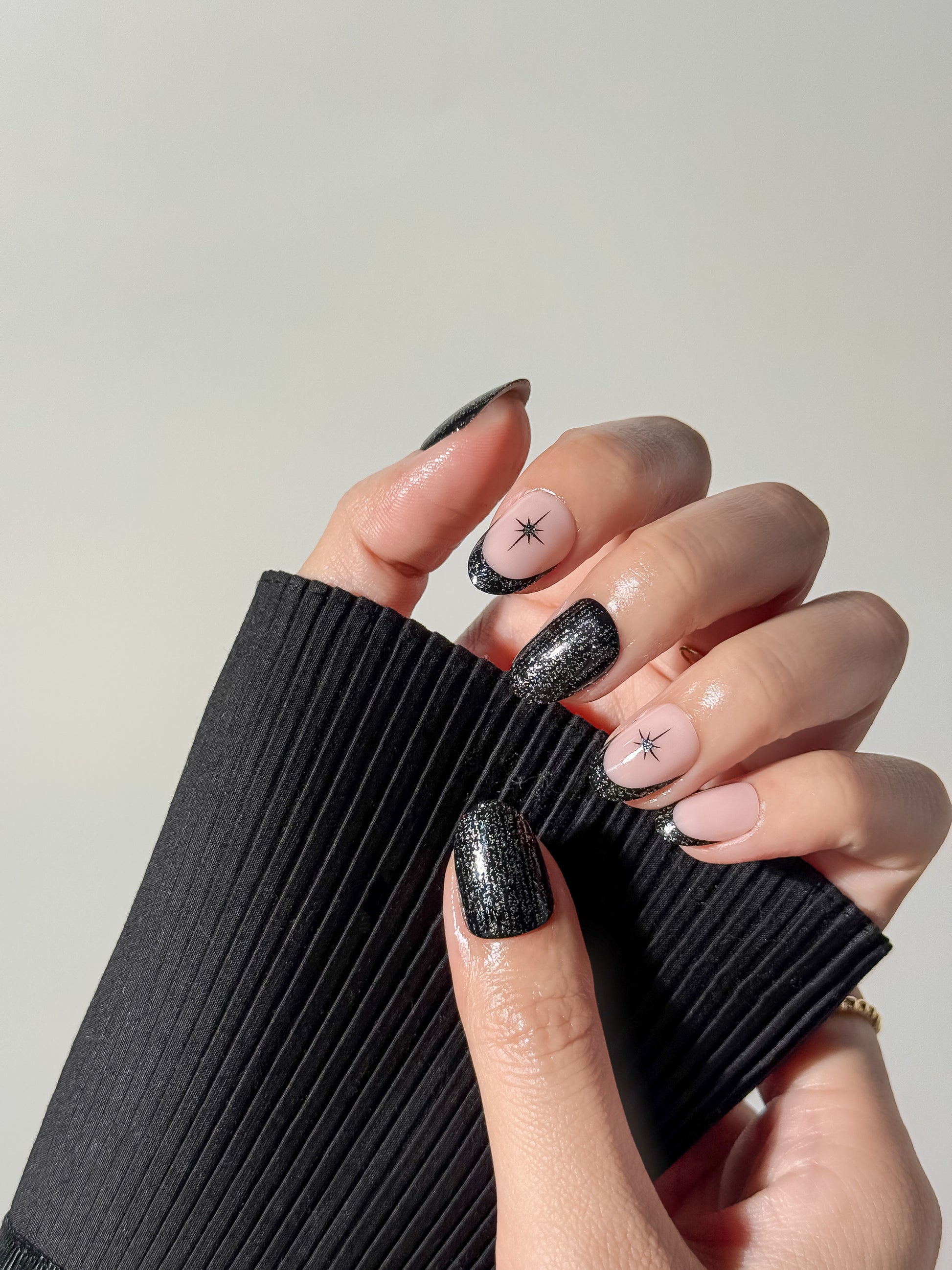 Close-up of a celestial-themed manicure featuring black shimmer accents and stars, styled with a black sleeve.