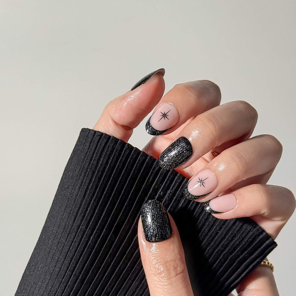 Close-up of a celestial-themed manicure featuring black shimmer accents and stars, styled with a black sleeve.