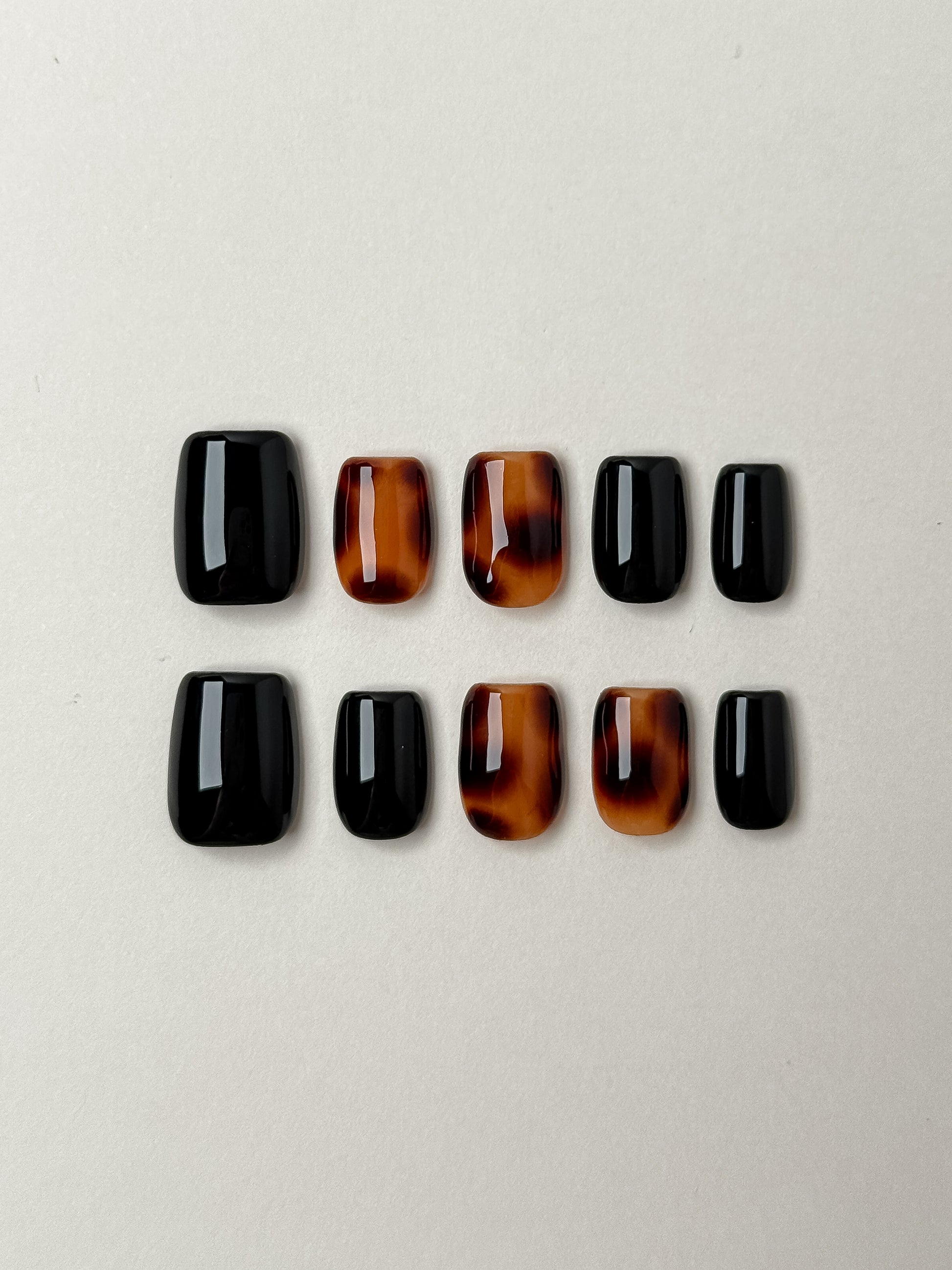 A 10-piece set of short square press-on nails featuring high-gloss black nails and traditional amber tortoiseshell accent nails.
