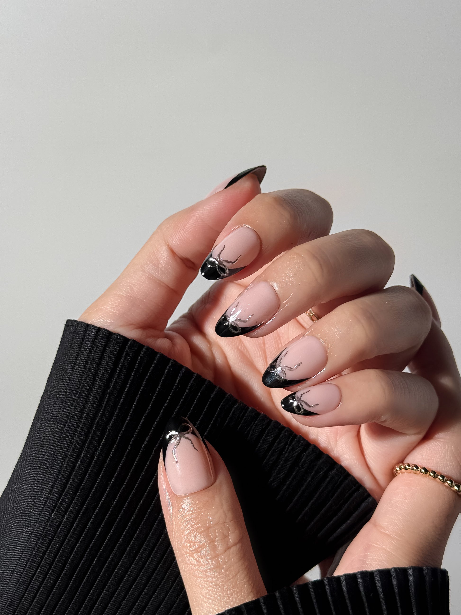 Close-up detail of a hand wearing the Silver Ribbon Noir manicure against a black ribbed sleeve.