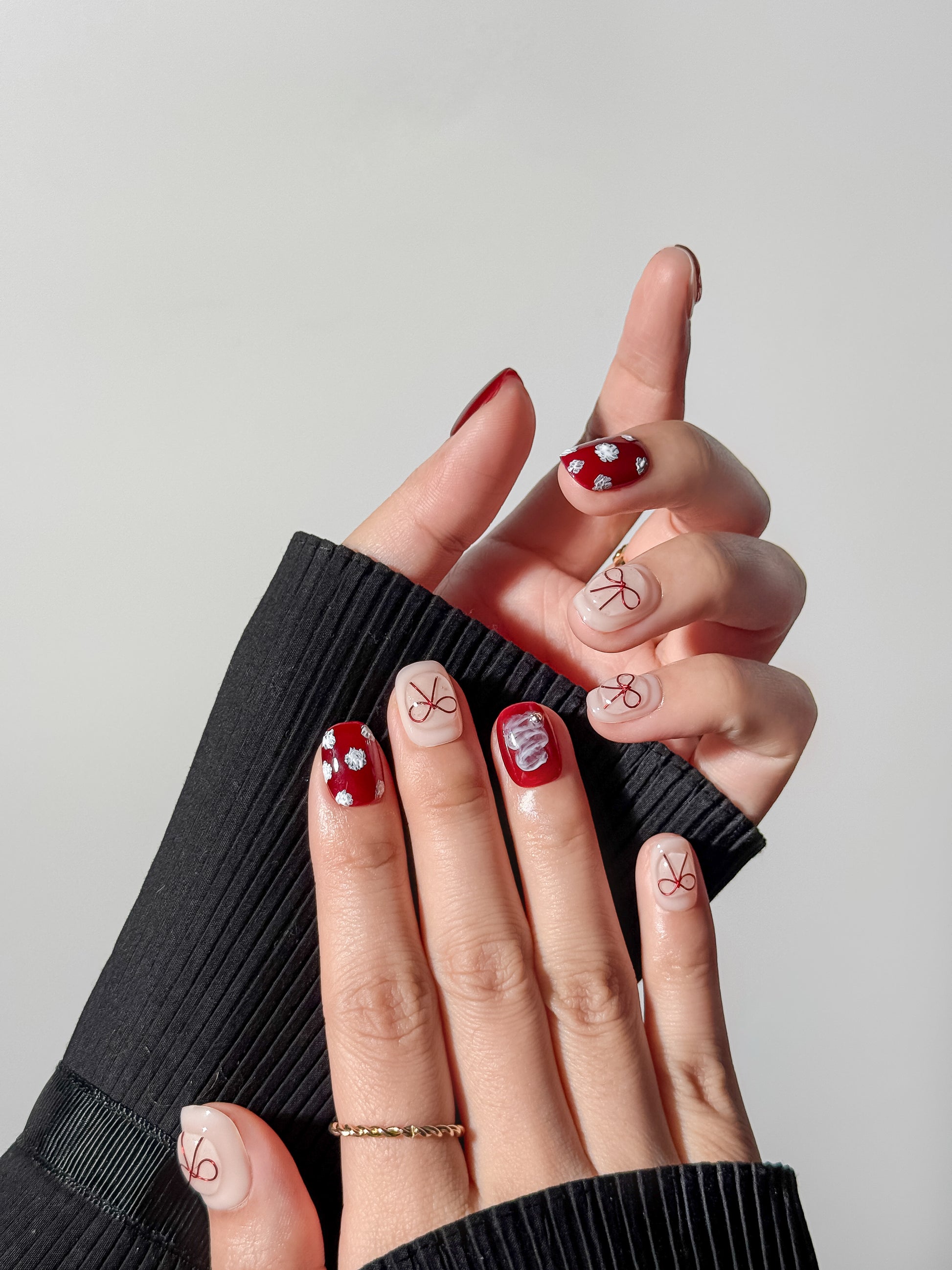 close-up of a hand wearing red bow nail art and white flower accents in a trendy balletcore aesthetic style