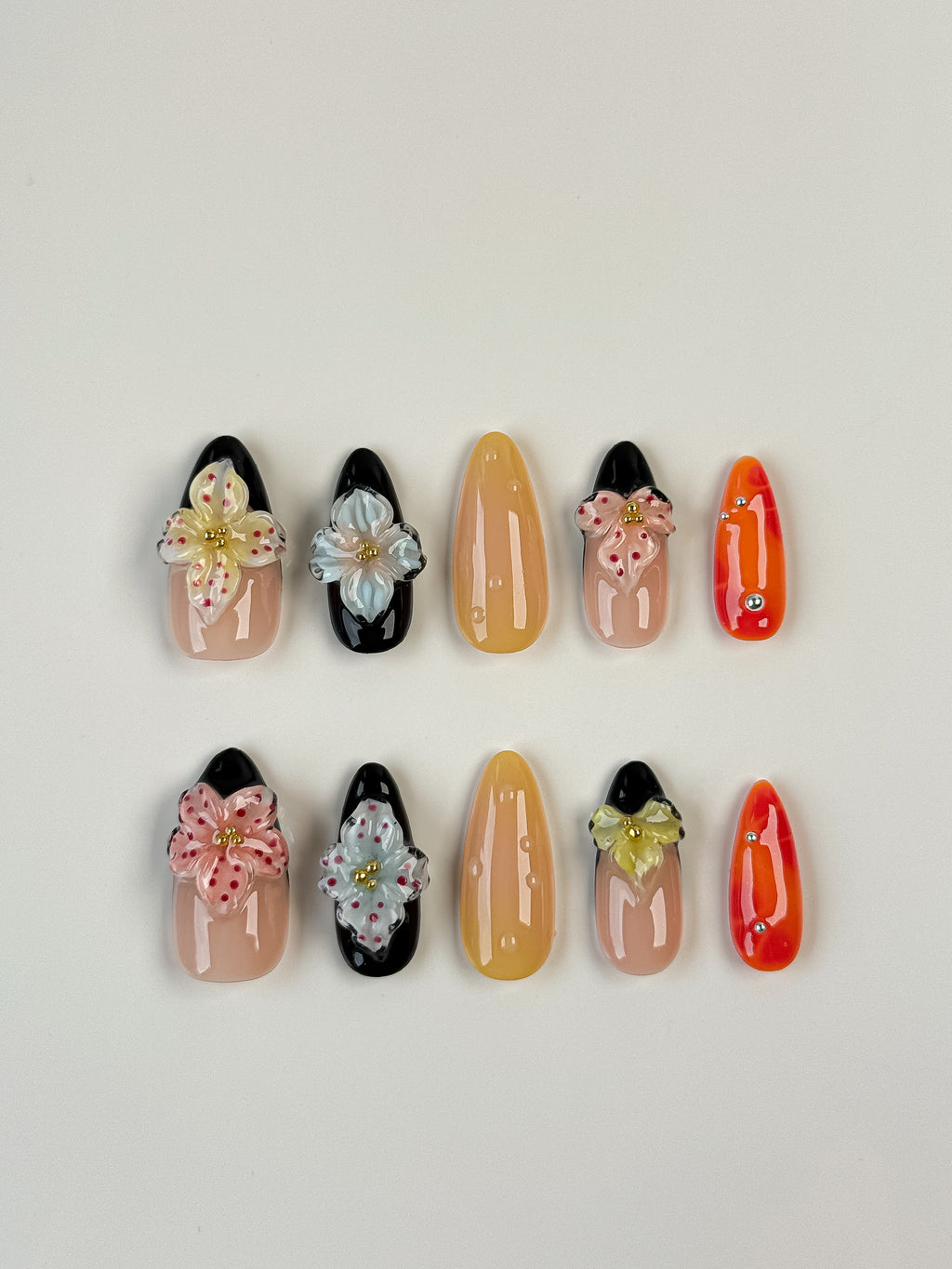 Almond-shaped tropical press-on nails with 3D floral designs in black, nude, orange and yellow colors – summer nail art set
