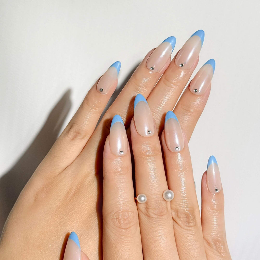 Elegant lifestyle shot of a woman's hands wearing handmade baby blue French tip nails with a glazed donut chrome effect, paired with a modern pearl ring.