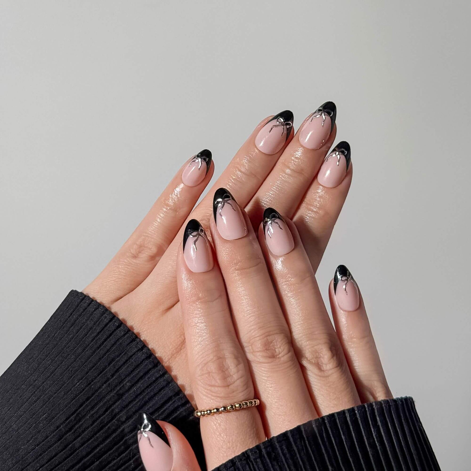 Handmodell zeigt den Coquette-Stil mit schwarzen French-Almond-Nägeln und silbernen Schleifen.