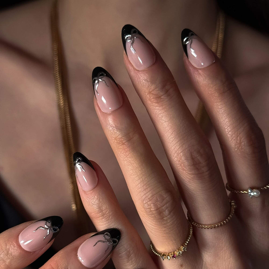 Model hand showcasing the press-on nails from Justmee with coquette aesthetic, black French tip almond nails and silver bows.