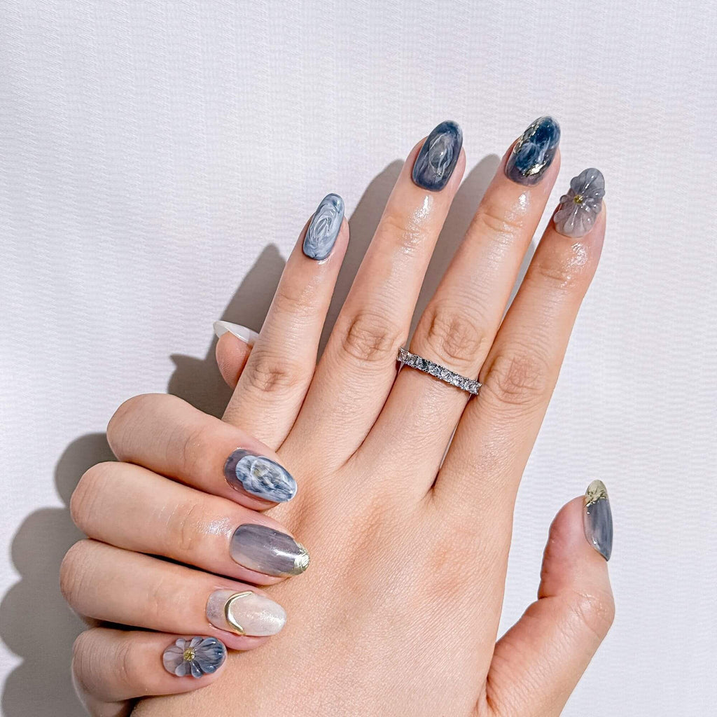 Lifestyle photo showcasing the Blue Mirage handmade nails, highlighting the elegant smoky marble texture and artisanal floral 3D art on a hand.