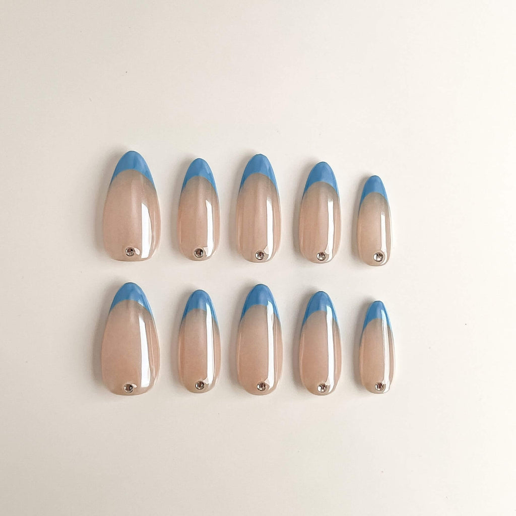Eine Produktübersicht von 10 handgefertigten Press-on-Nägeln in Mandelform mit hellblauen French-Tips, schimmerndem Chrome-Finish und einem silbernen Schmuckstein am Nagelansatz.