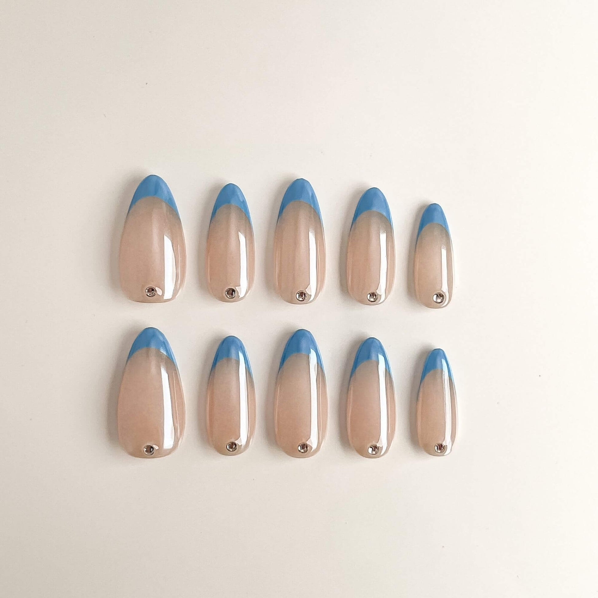 Eine Produktübersicht von 10 handgefertigten Press-on-Nägeln in Mandelform mit hellblauen French-Tips, schimmerndem Chrome-Finish und einem silbernen Schmuckstein am Nagelansatz.
