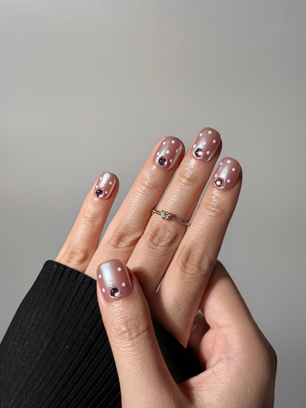 Hand wearing Justmee blush shimmer press-on nails with dots and gems in short square style