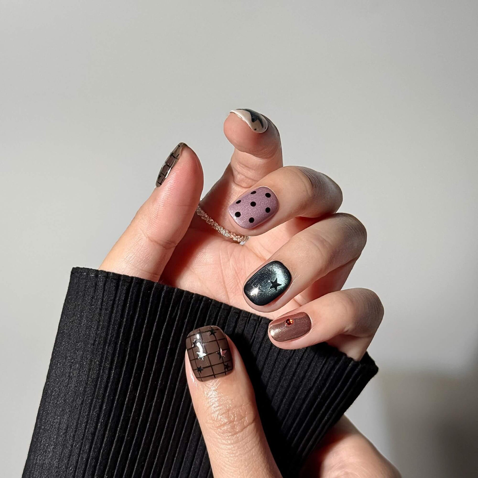 Detailed lifestyle shot of a hand wearing Celestial Grunge press-on nails, highlighting the shimmering cat-eye effect and metallic copper accents.