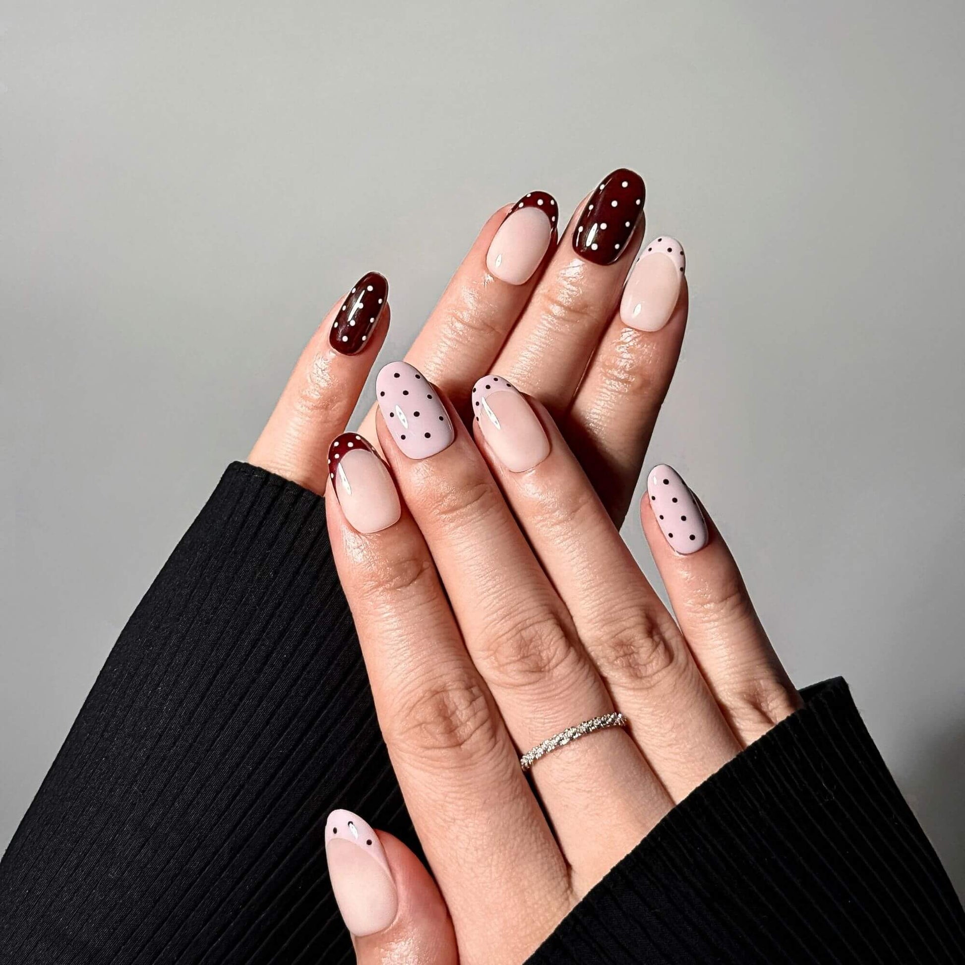 Professional photography of hands wearing the Cocoa Dot mix-and-match press-on nails, paired with a black ribbed sweater for a cozy, elegant look