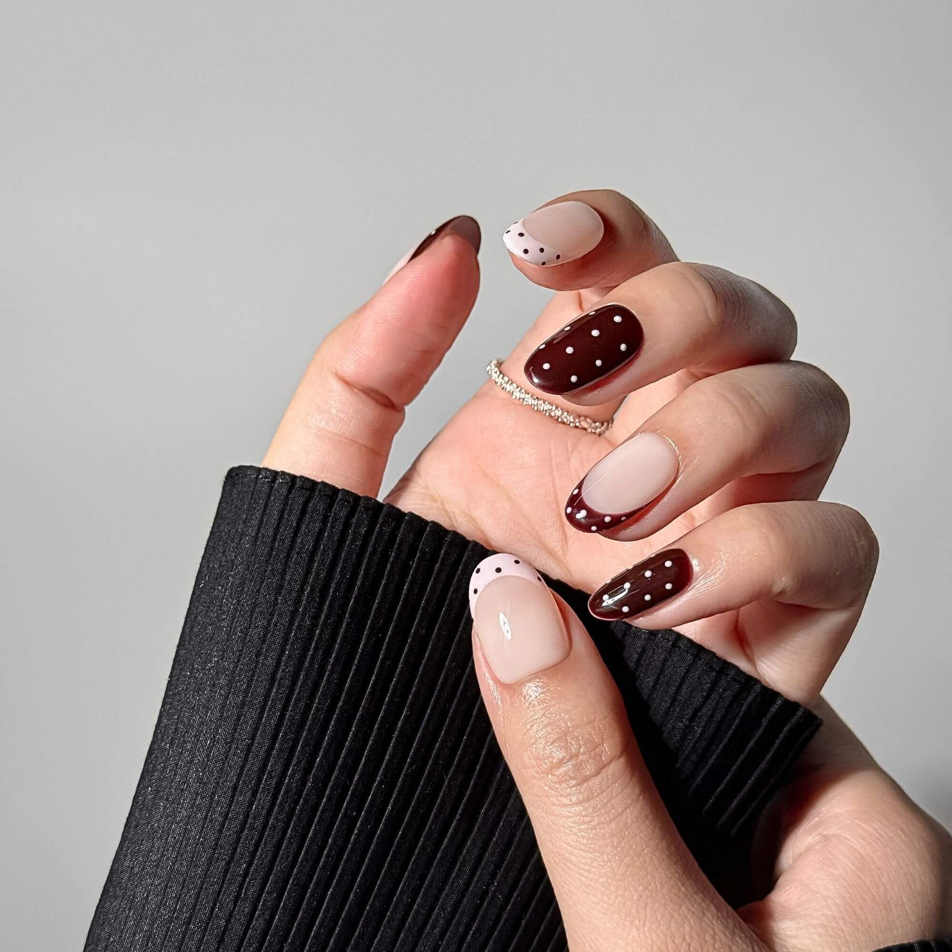 Detailliertes Lifestyle-Foto einer Hand mit Cocoa Dot Kunstnägeln, das das hochglänzende schokobraune Finish und die zarten weißen Punkte hervorhebt.