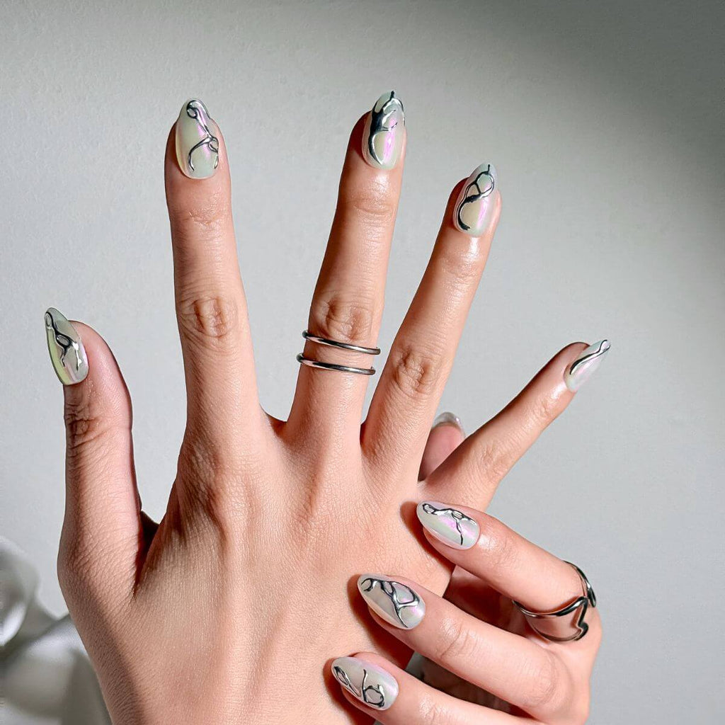 Nahaufnahme einer Hand mit mandelförmigen Press-on Nails, verziert mit 3D-Flüssigmetall-Design und passenden silbernen Ringen für einen modernen Cyber-Look.