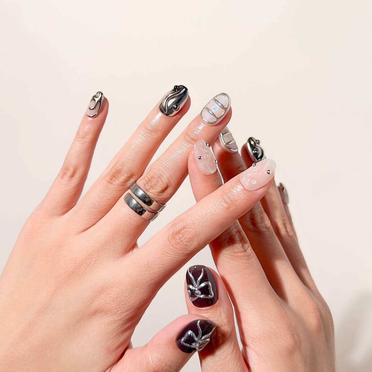 Nahaufnahme von justmee Gel-Nägeln zum Aufkleben an einer Hand mit Silberringen. Das kurze, eckige Design vereint schwarze und silberne Chrome-Nägel mit moderner 3D-Nailart für eine professionelle Maniküre zum Selbermachen.