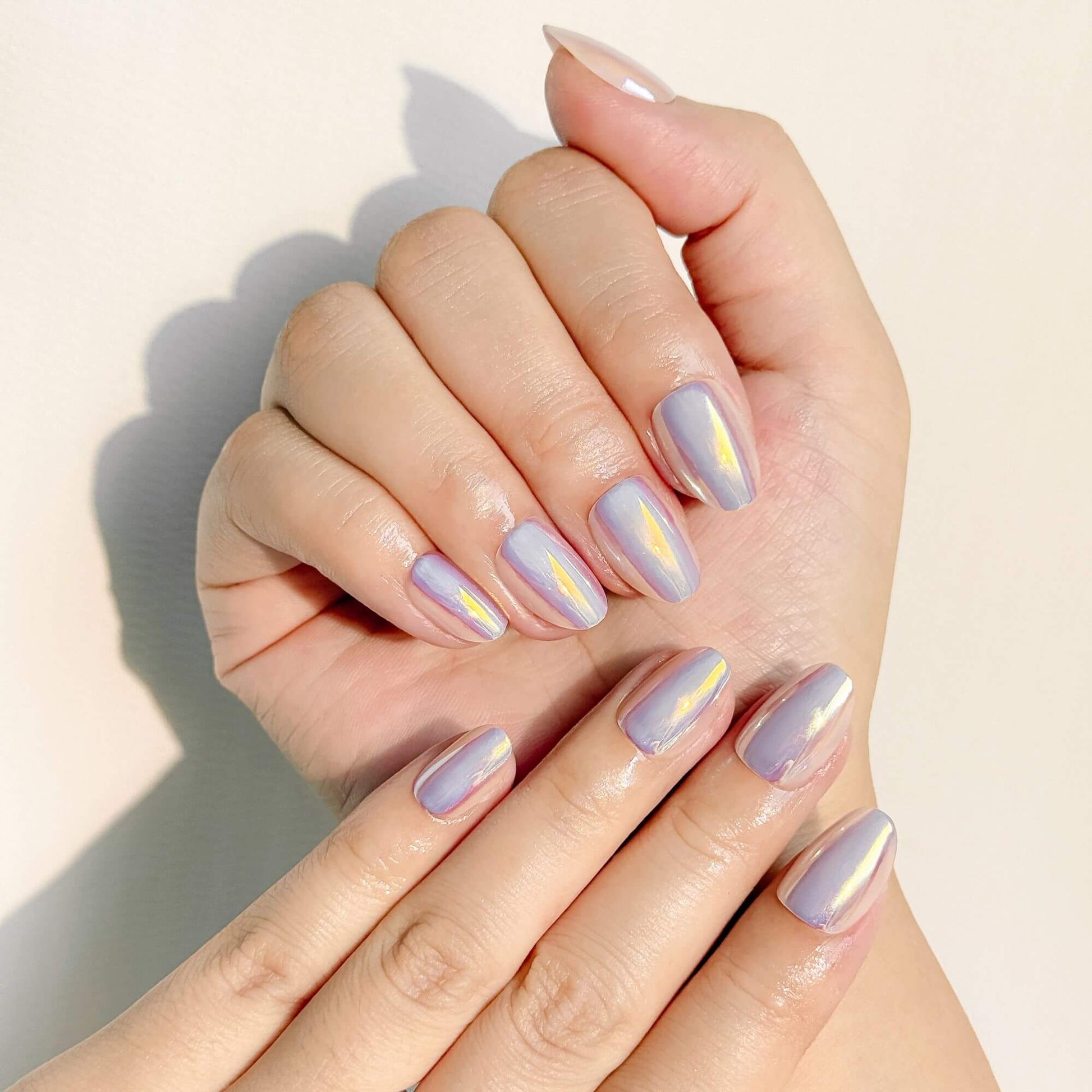 Close-up of a person's hands wearing short oval iridescent chrome nails, showcasing the "glazed donut" effect and smooth glossy texture in natural light