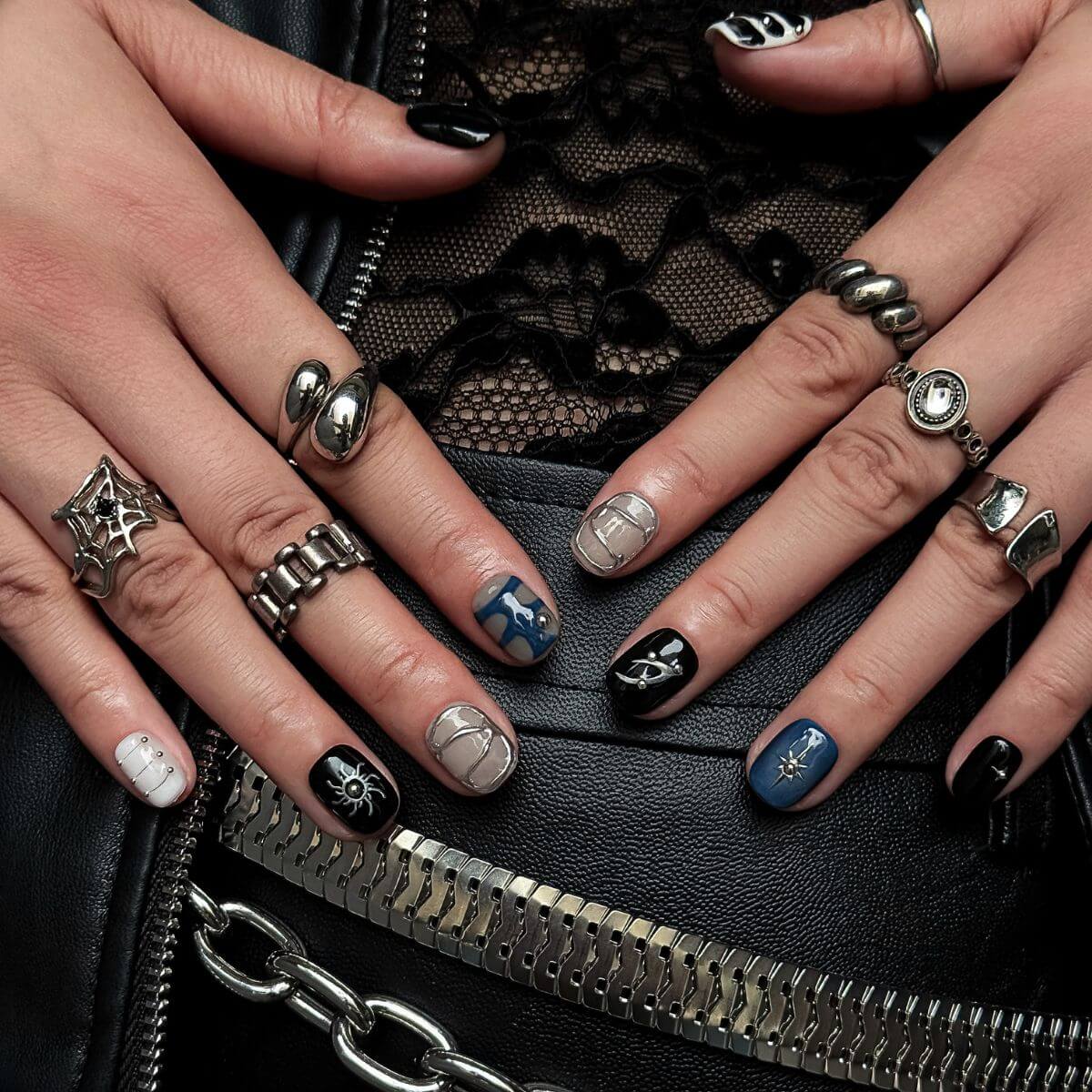 Model hands resting on a black leather bag showcasing gothic grunge press-on nails with spider graphics, dark blue marble, and heavy 3D metallic silver framing.