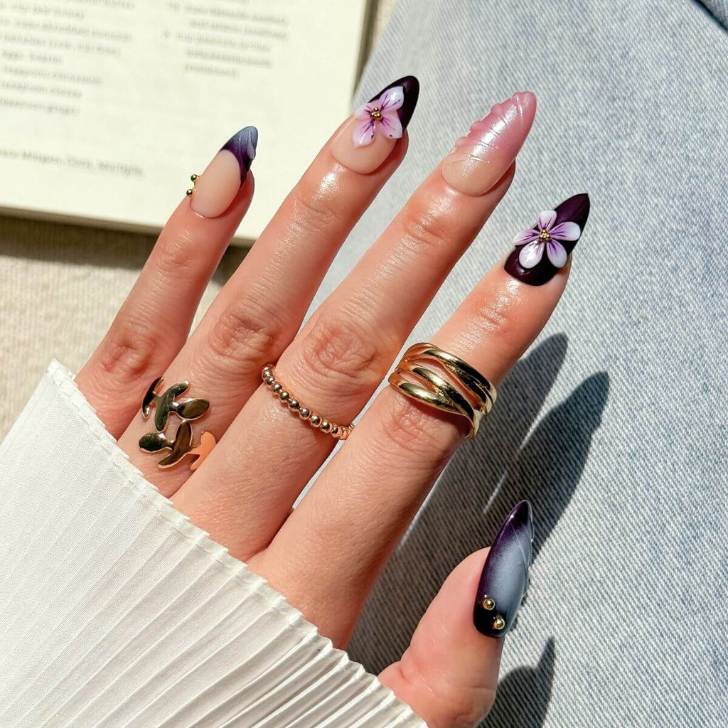 Ein Lifestyle-Foto einer Hand mit magnetischen violetten künstlichen Fingernägeln und Ringen, fotografiert im Alltag vor einem Jeansstoff.