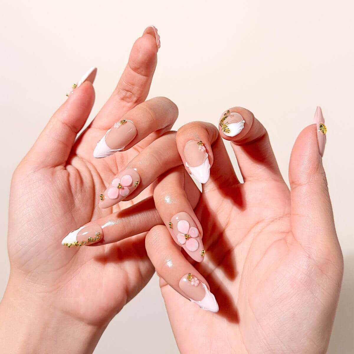 Elegant lifestyle shot showing two hands interlaced, showcasing a full set of milky pink artificial nails with intricate 3D flowers and romantic mermaid-core textures.