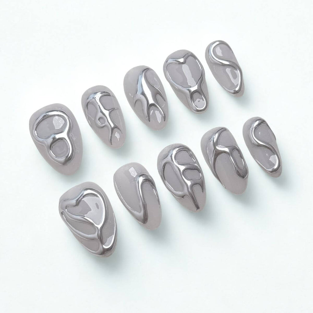 Flatlay von 10 justmee Kunstnägeln in Mandelform. Milching-graues Gel-Design mit 3D Chrome Liquid Metal Effekten für eine moderne Maniküre zum Selbermachen.
