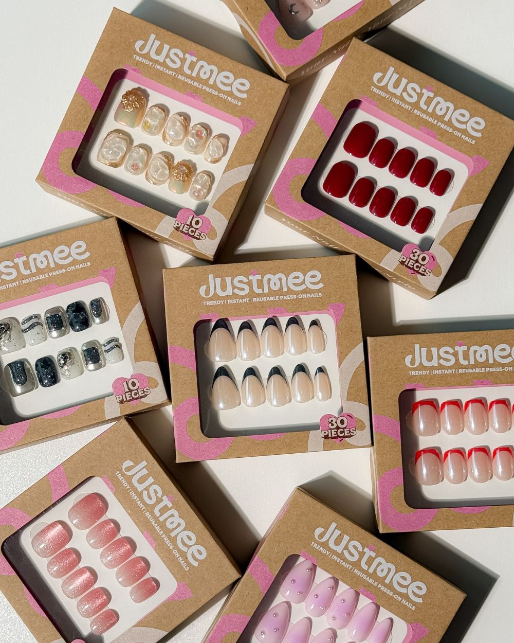 An assortment of Justmee luxury reusable press-on nail sets in eco-friendly branded packaging, featuring handmade and salon-quality designs.