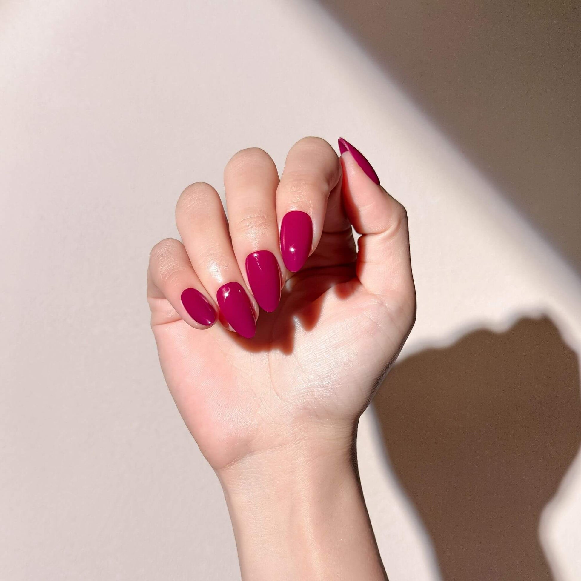 Eine Hand mit trendigen magenta Press-on-Nägeln in Mandelform.