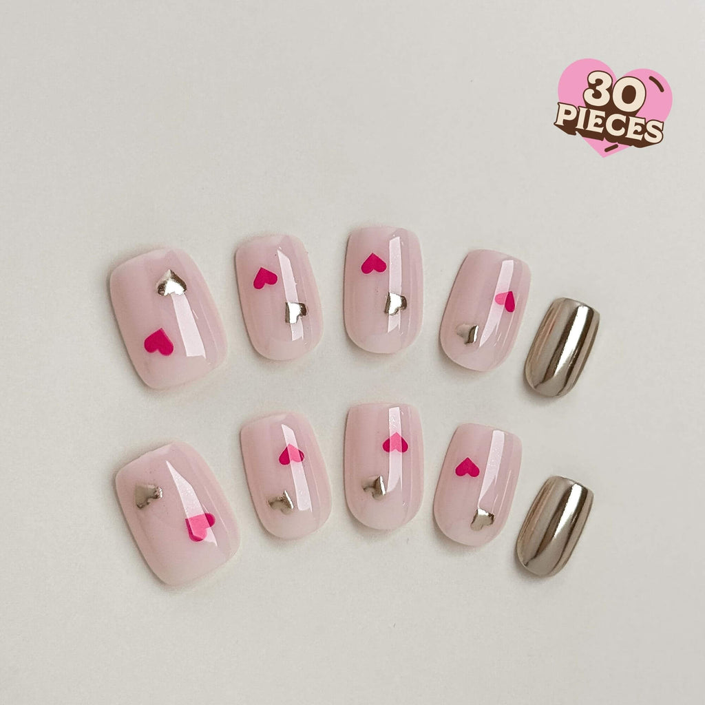 Eine Flachansicht von kurzen, eckigen Press-on-Nägeln mit milchig-rosa Basis, pinken und silbernen Chrom-Herzen sowie vollflächigen silbernen Metallic-Akzentnägeln.
