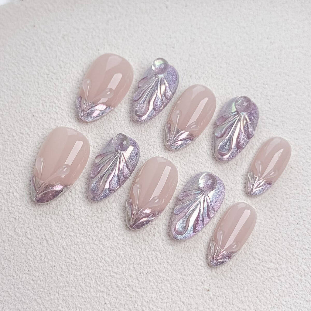 Studio flat lay of premium medium almond press-on nails featuring a nude base, shimmering purple magnetic cat-eye gel, 3D sculpted texture seashell patterns, and liquid water droplets.