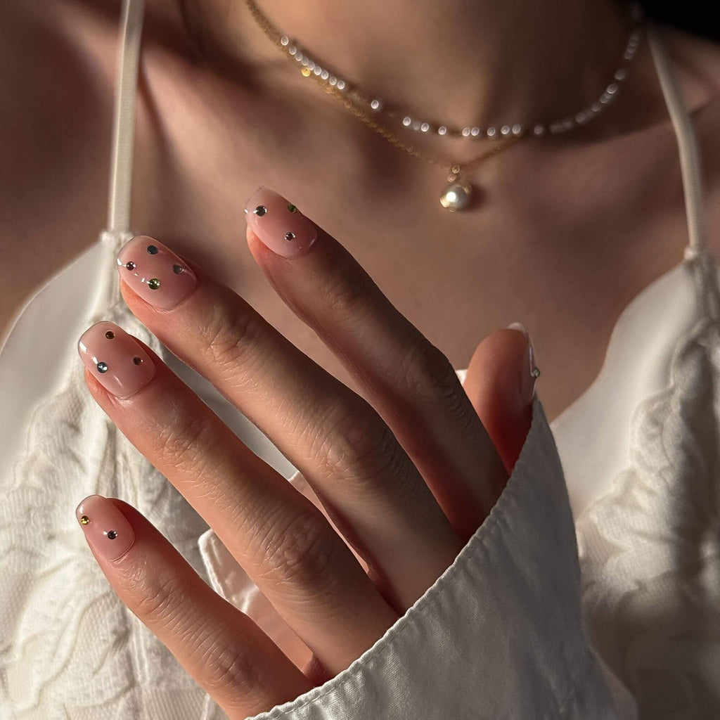 Ein inspirierendes Lifestyle-Foto der Prism Petal Strass-Kunstnägel, kombiniert mit einer weißen Spitzenbluse und Perlenschmuck für einen hochwertigen, eleganten Look.