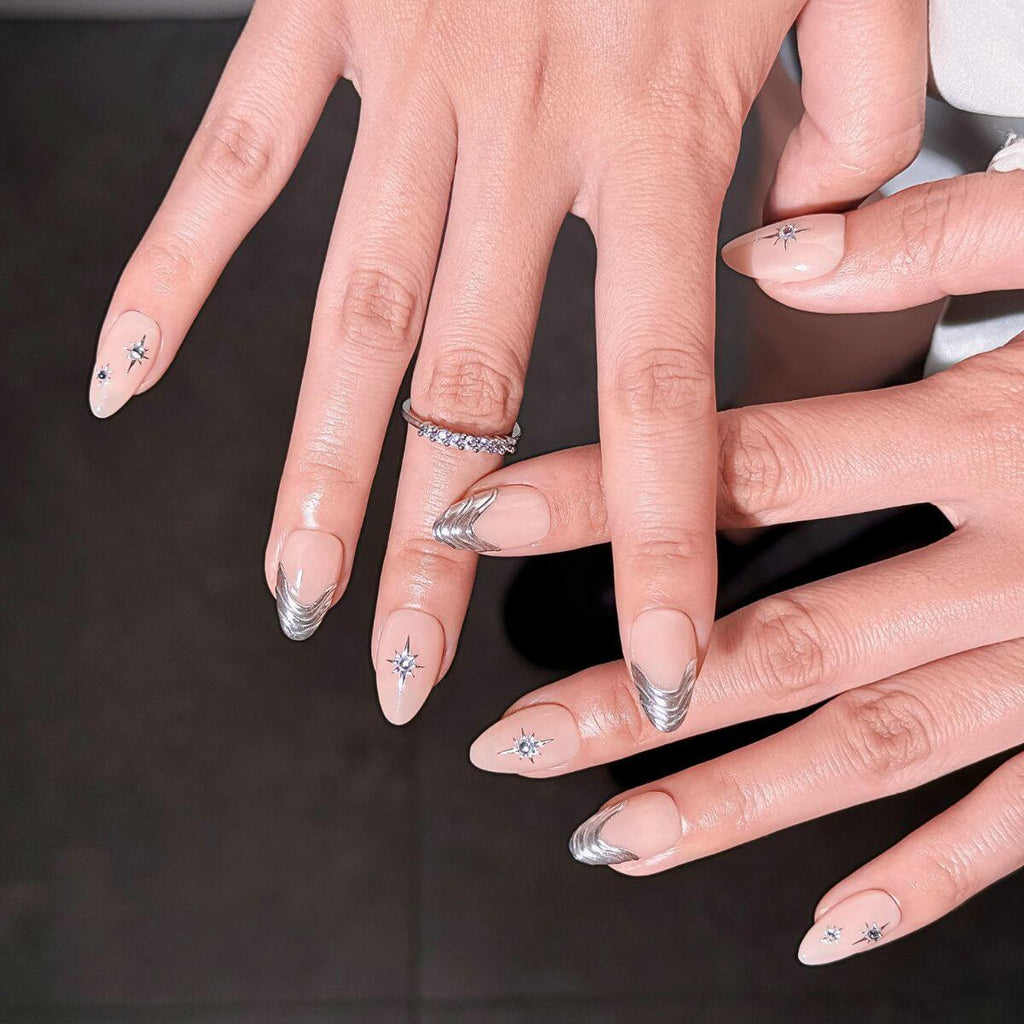 Nahaufnahme einer makellosen Balletcore Press-On Maniküre in Mandelform mit strukturierten silbernen Y2K-Metallic-Linien und kleinen Strasssteinen auf dunklem Hintergrund.