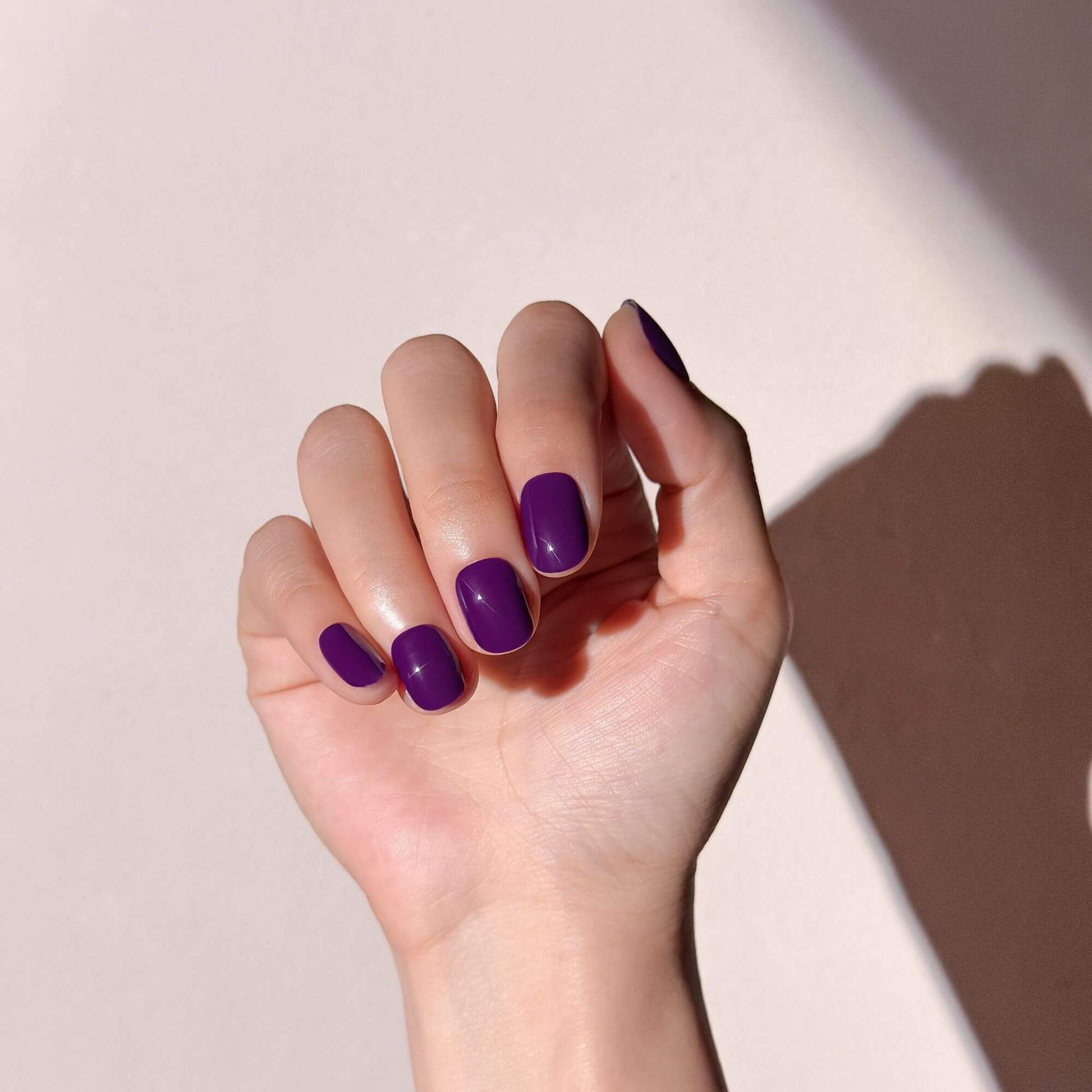 Handmodell mit eleganten, pflaumenvioletten Hochglanz-Kunstnägeln.