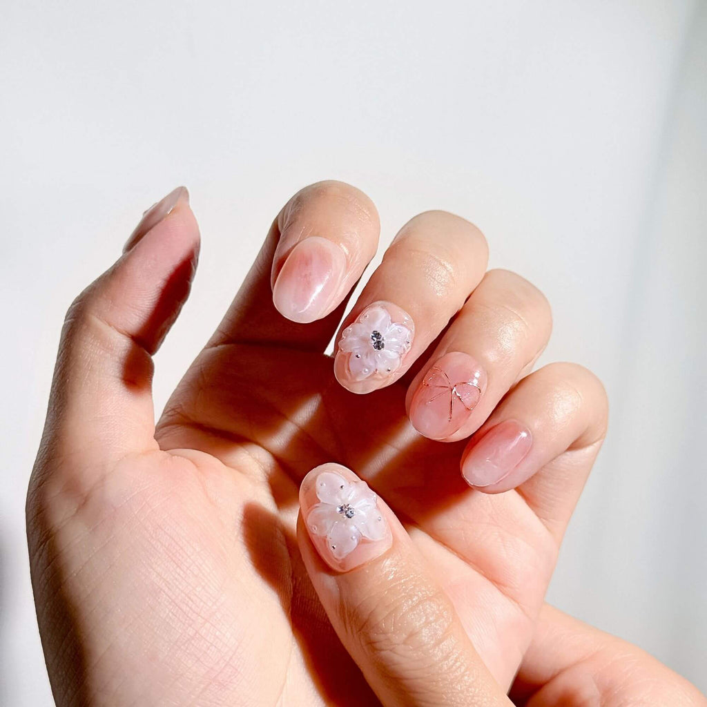 Close-up of a hand wearing pink marble press-on nails, highlighting the intricate 3D floral charms and the glossy, high-shine finish.