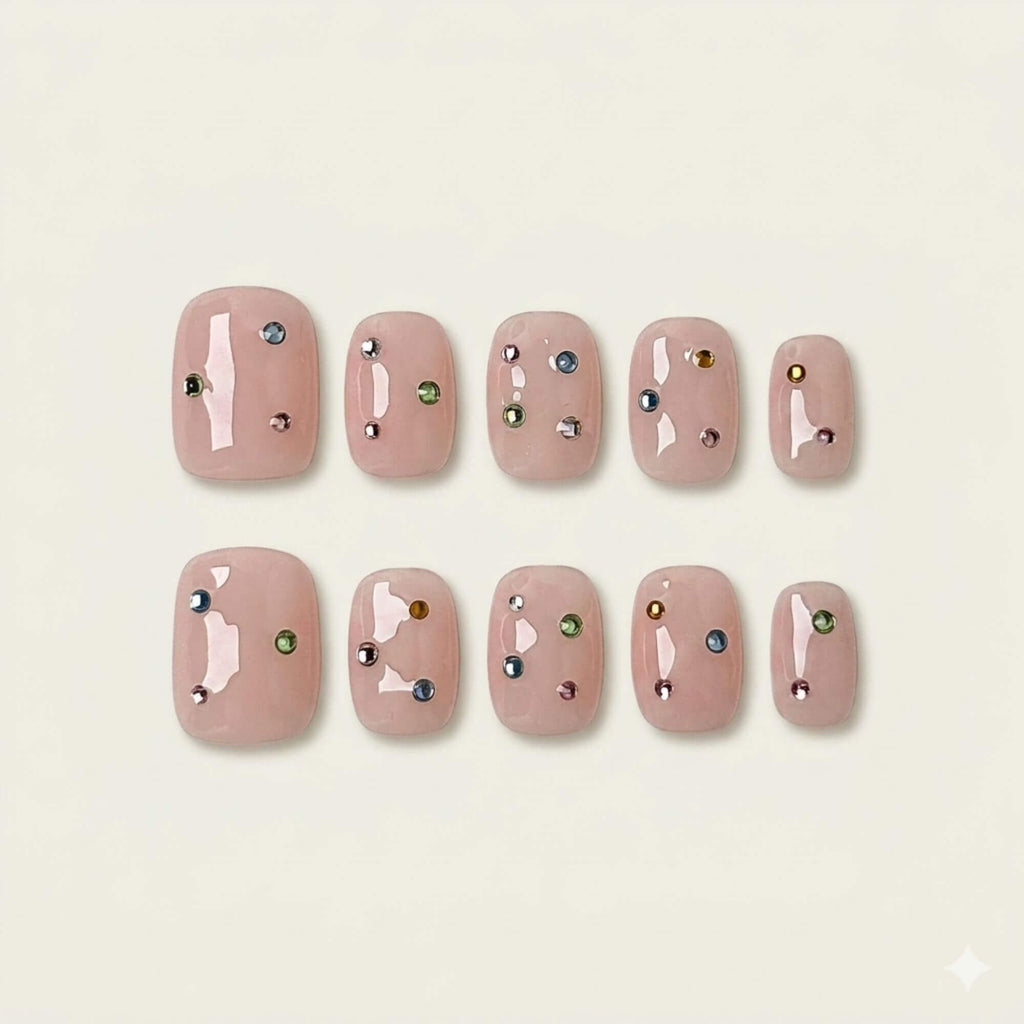 A flat lay display of 10 handmade short square press-on nails from the Prism Petal collection, featuring a sheer nude pink base and delicate multi-colored rhinestone accents.