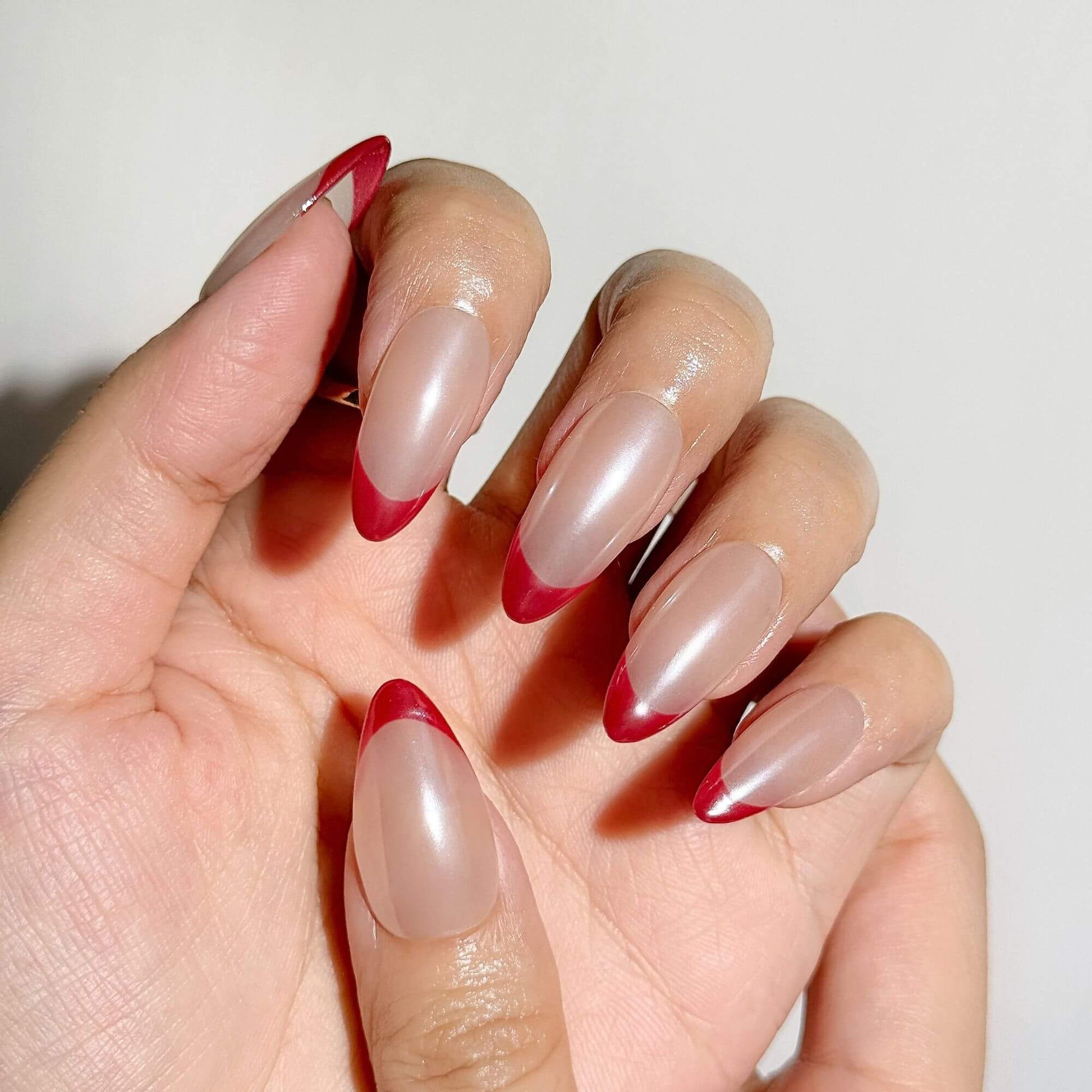 Detailansicht handbemalter Press-on Nails in Mandelform mit irisierendem Perlmutt-Chrome-Glanz und präzisen roten French-Spitzen.