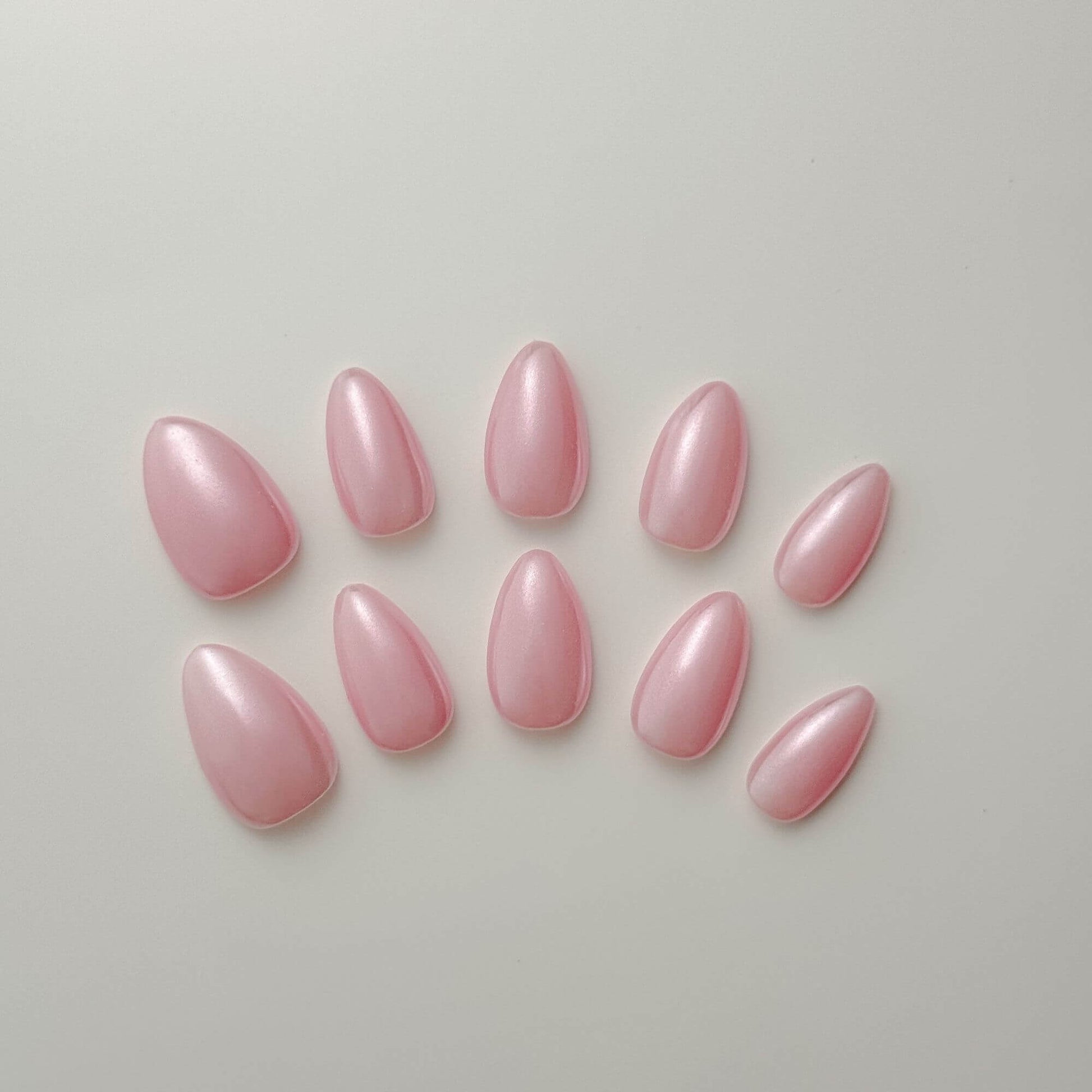 Eine Produktübersicht von 10 handgefertigten Press-on-Nägeln in Mandelform in zartem Aurora-Rosa mit einem schimmernden Perlmutt-Chrome-Finish.