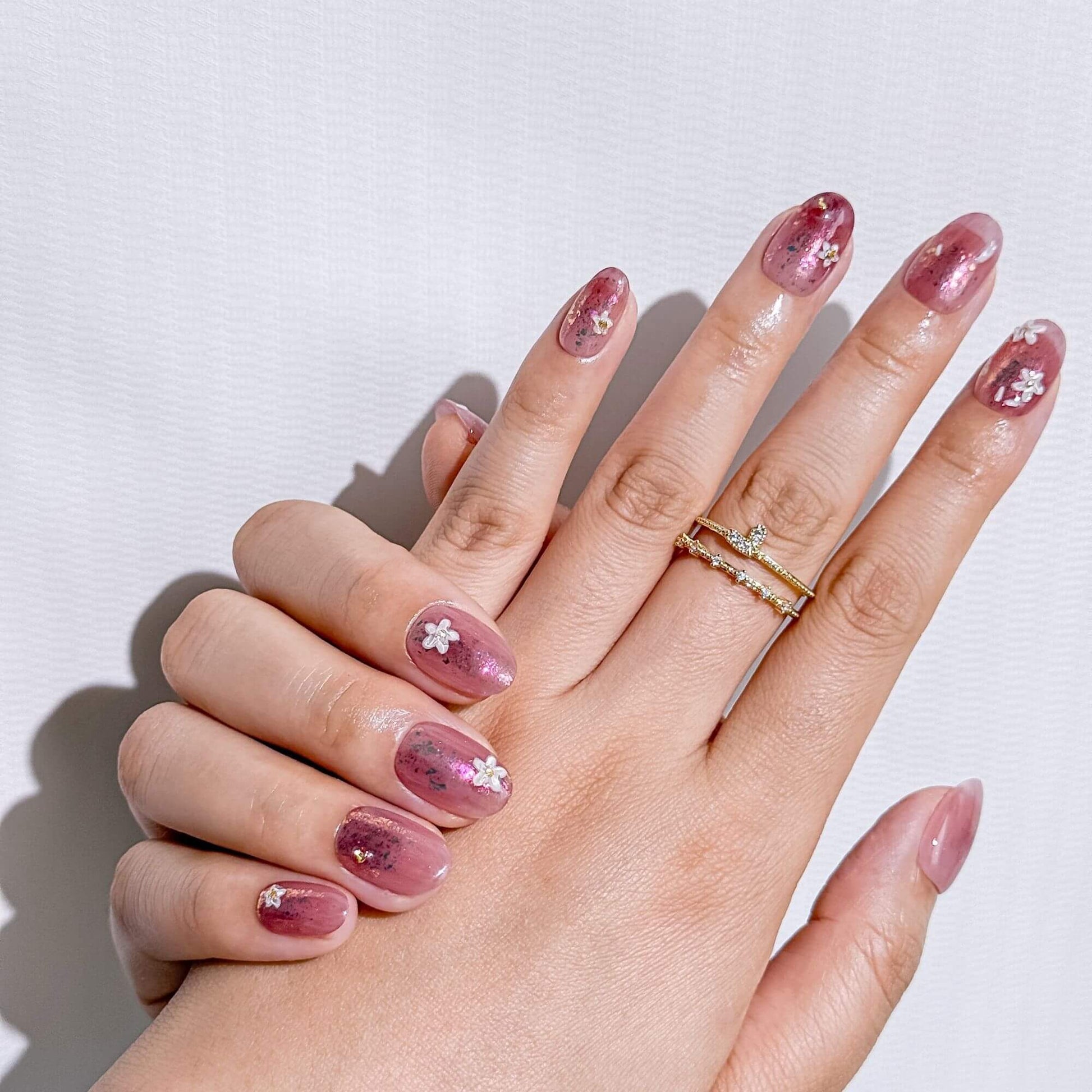 Elegante Lifestyle-Ansicht von handgefertigten Rosenquarz-inspirierten Press-on Nails mit Blumen, kombiniert mit filigranen Goldringen für einen professionellen Look.