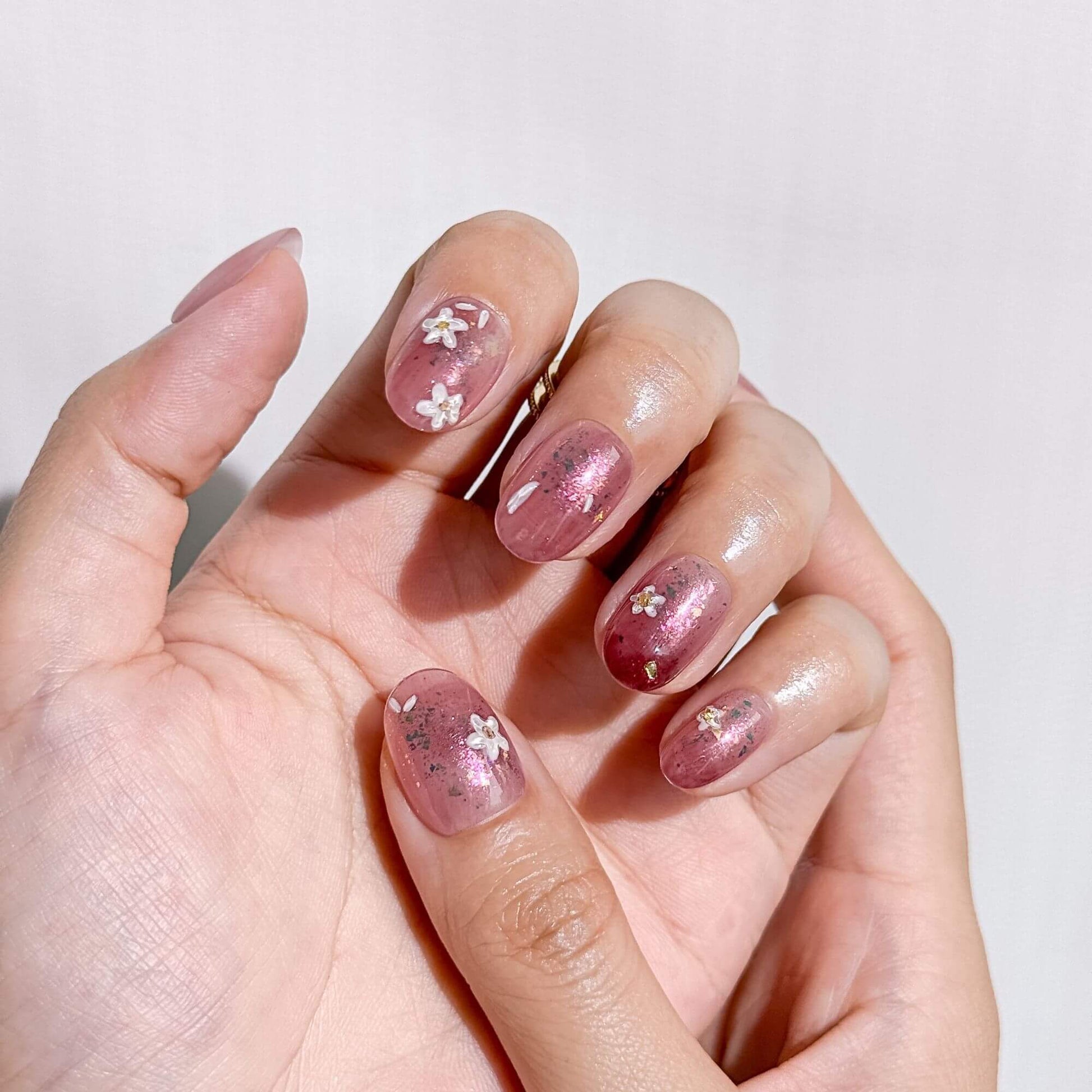 Nahaufnahme einer Hand mit handgefertigten rosa Jelly-Nägeln, verziert mit aufwendiger Blumenkunst und schimmernden Gold-Details.