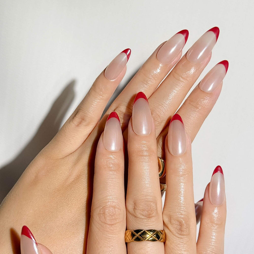 Lifestyle-Foto von handgefertigten roten French-Chrome-Nägeln an einer Hand mit Goldring für eine luxuriöse Maniküre.