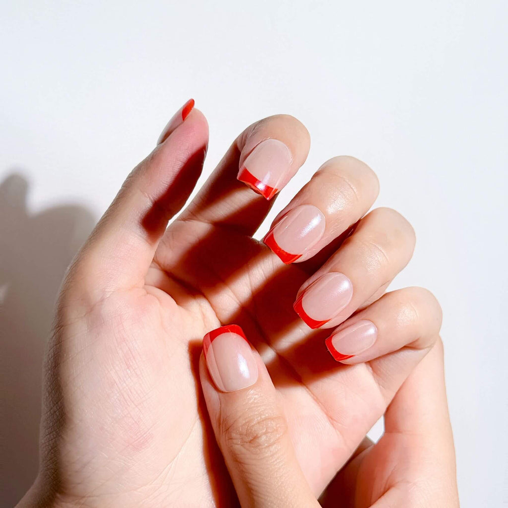 Hands wearing Justmee short red French tip press-on nails, showing an elegant and classic French manicure with a natural fit.