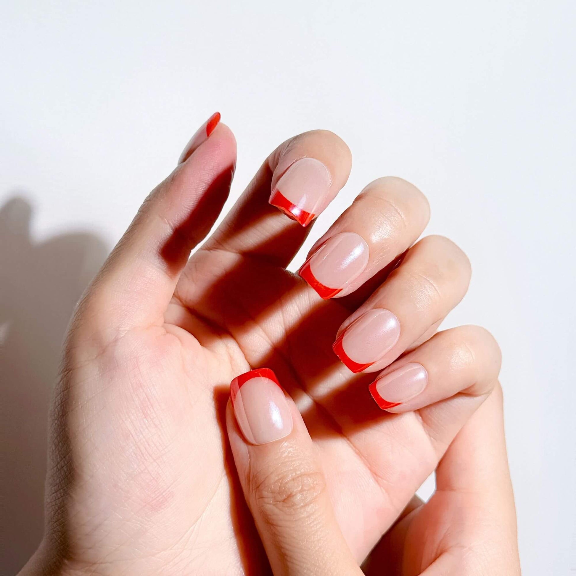 Hands wearing Justmee short red French tip press-on nails, showing an elegant and classic French manicure with a natural fit.