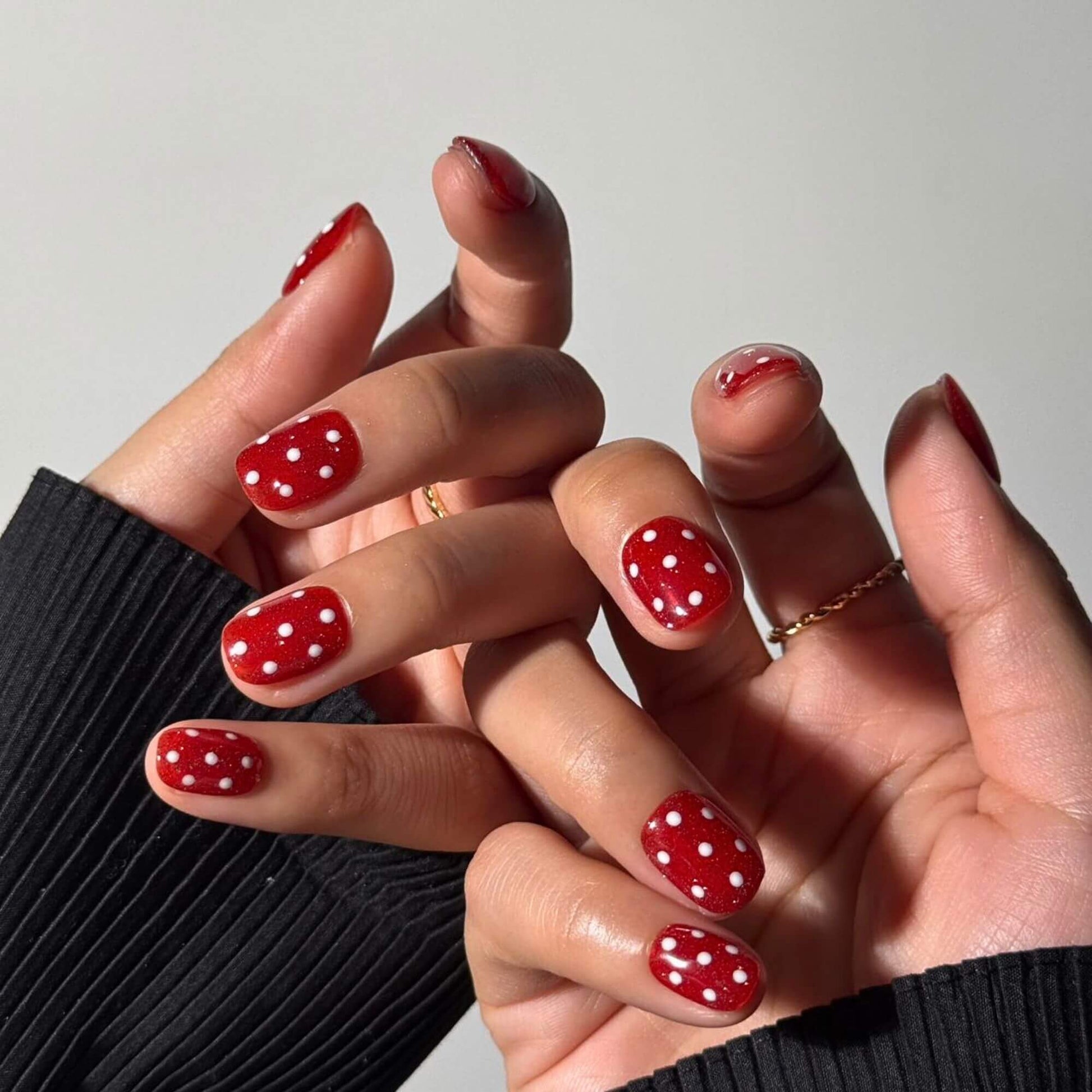 Lifestyle photo of a woman's hands wearing the Ruby Retro Red handmade nails, showcasing the vibrant red shimmer and retro polka dot design against a black sweater.
