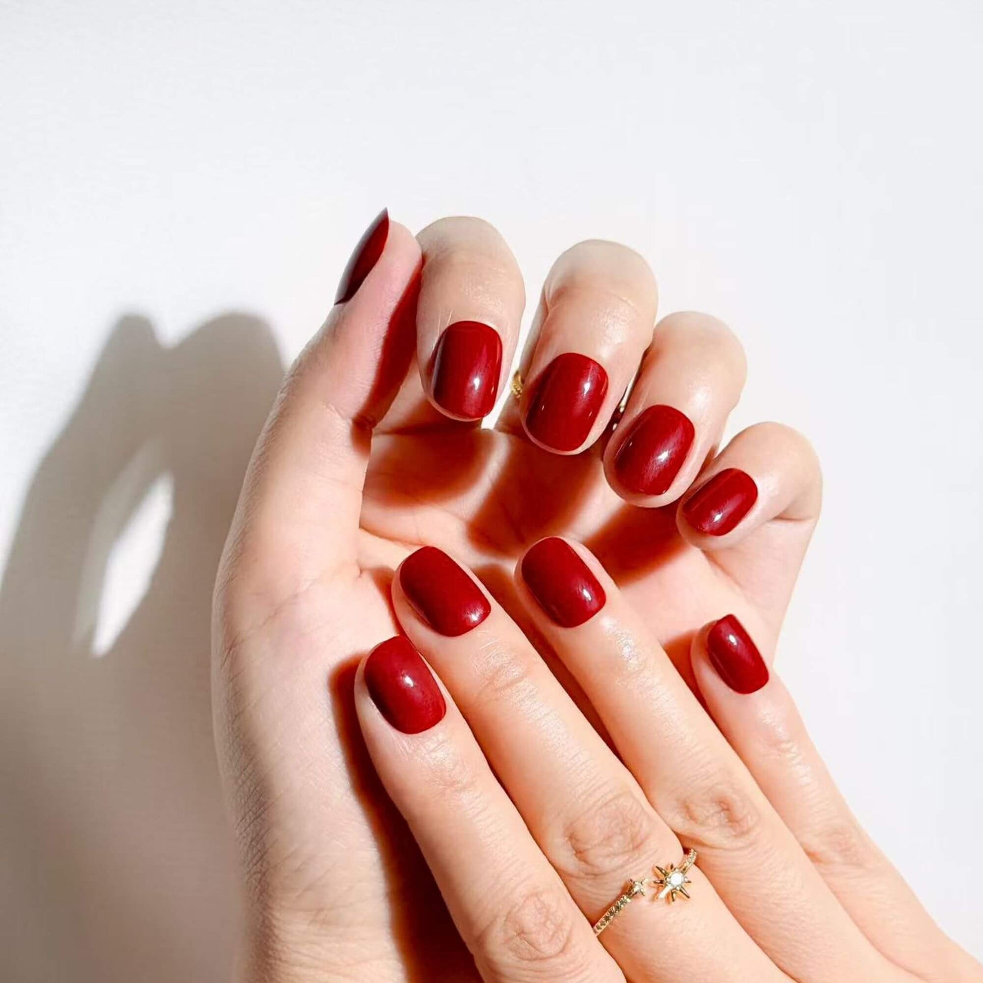 Elegante Hände mit weinroten kurzen Press-on-Nägeln von Justmee, die eine perfekte Passform und einen klassischen, anspruchsvollen Maniküre-Look zeigen.