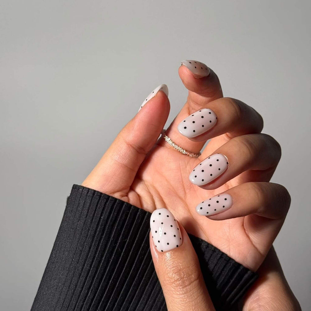 Lifestyle photo of a hand wearing Noir Dots handmade nails, showcasing the elegant oval shape and timeless polka dot pattern paired with a delicate diamond band.