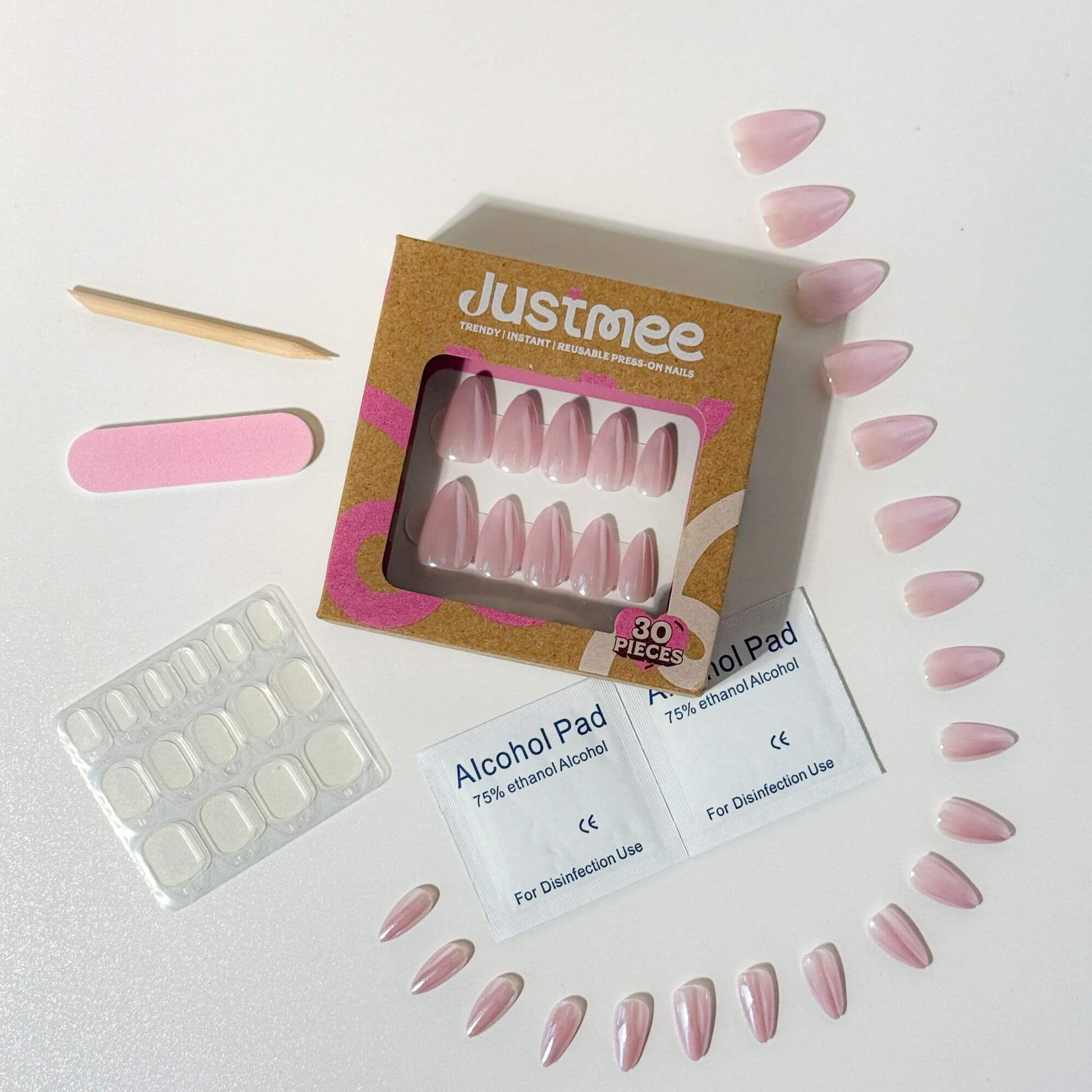 Ein komplettes Justmee Press-on-Nagel-Set mit 30 perlrosa Mandelnägeln, Klebepads, Reinigungstüchern und Feile, angeordnet um die umweltfreundliche Verpackung.