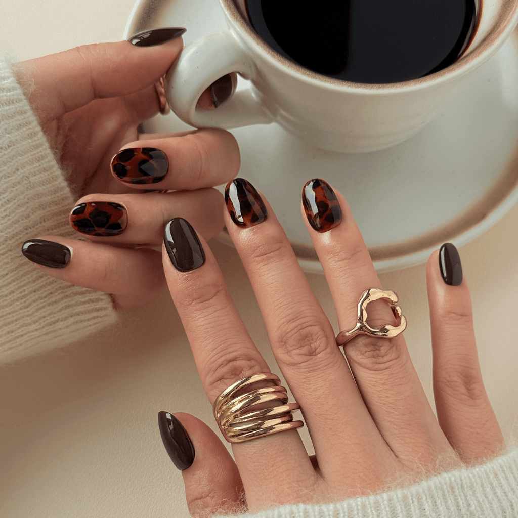 Model holding a white coffee cup wearing short oval dark brown tortoise shell stick-on nails with gold rings.