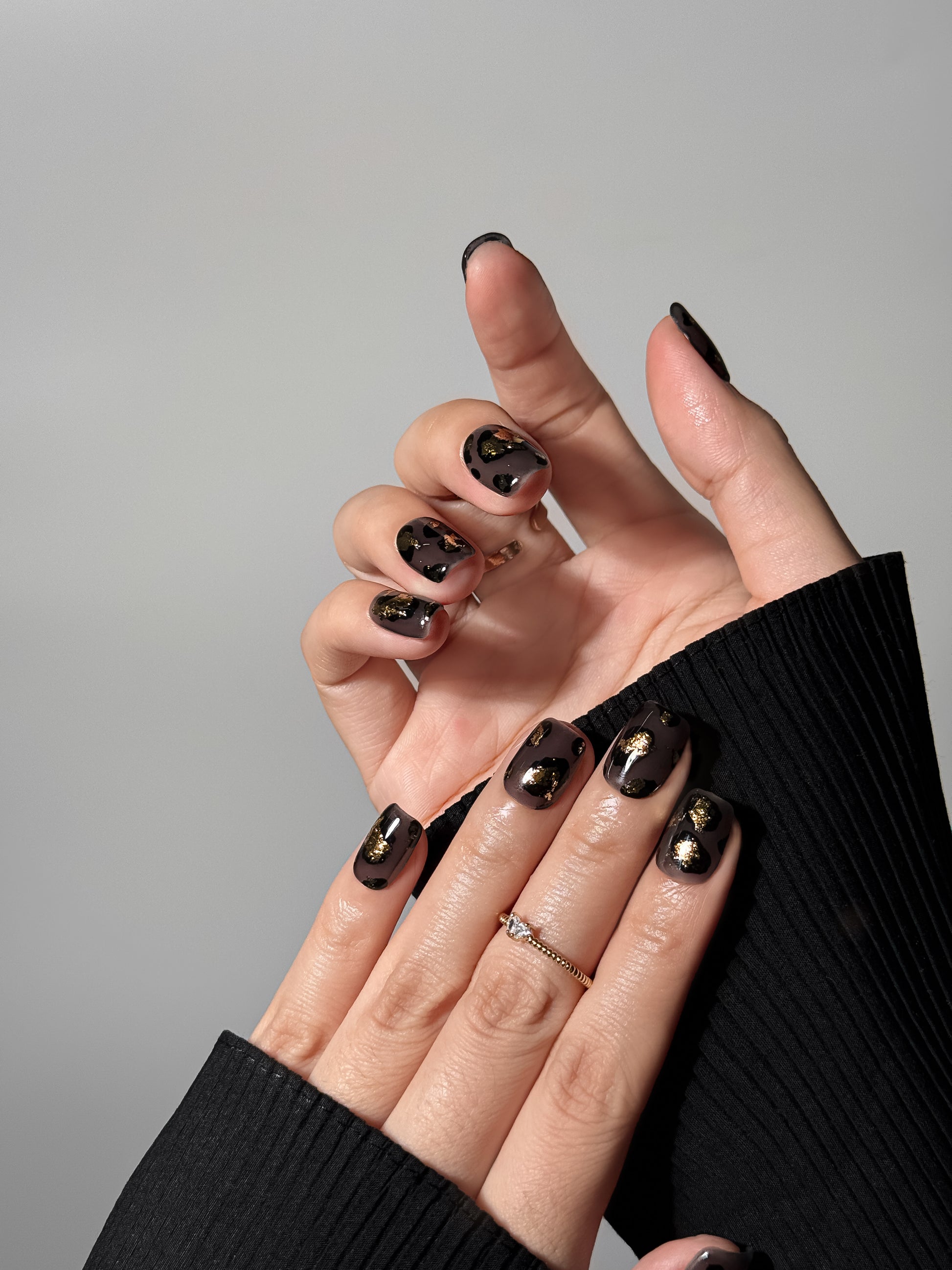 High-gloss leopard print manicure with gold leaf accents styled with a black sweater, emphasizing a chic and moody nail aesthetic.