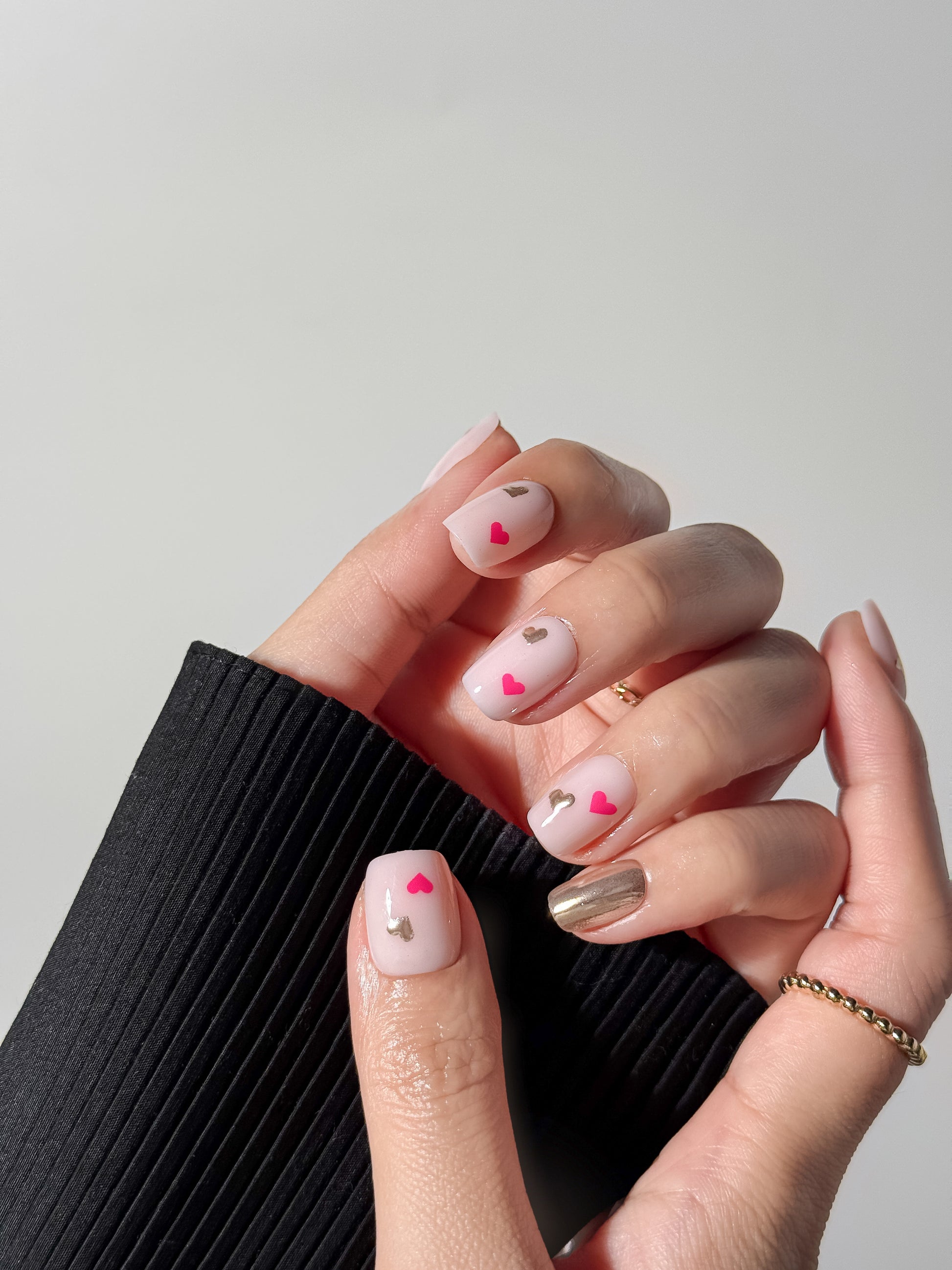 Close-up of a hand wearing short square milky pink nails decorated with tiny silver and hot pink hearts.